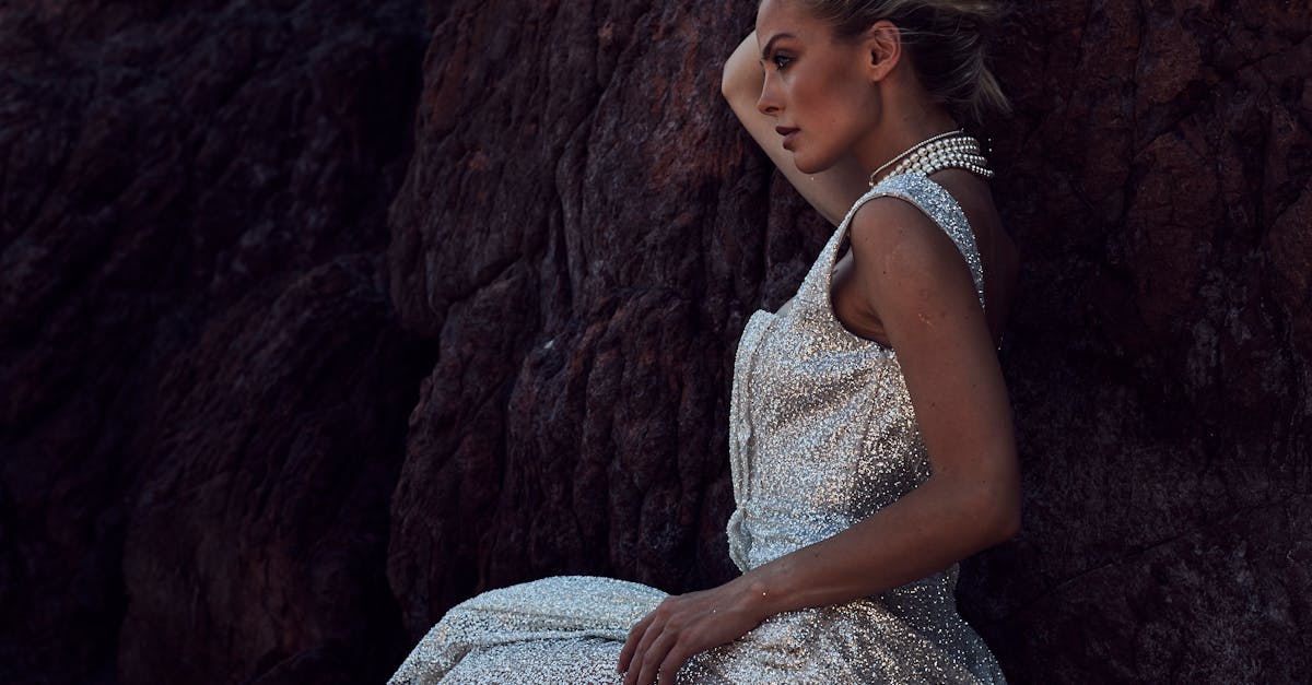 A stunning woman in a sparkly gown poses dramatically against rugged rocks.