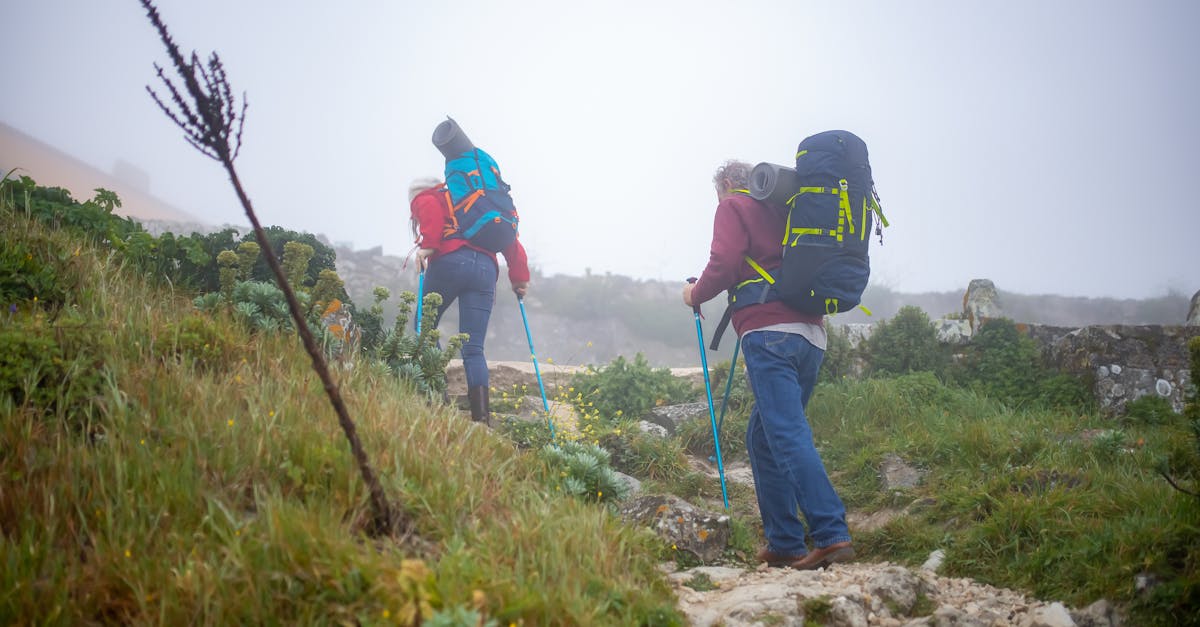 A senior couple enjoys a misty hike in Portugal, each carrying backpacks and walking sticks.