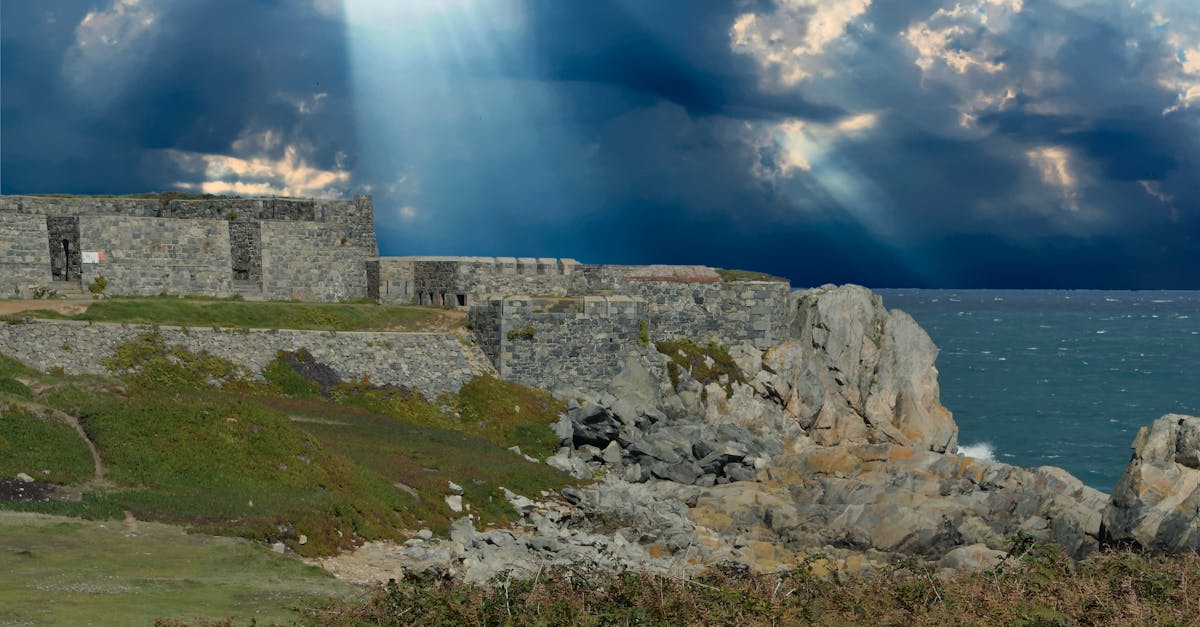 Rugged fort along Guernsey's rocky coast with dramatic clouds and sunrays breaking through.