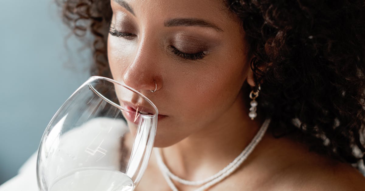 Close-up portrait of a black woman savoring a glass of white wine, eyes closed, exuding grace and beauty.