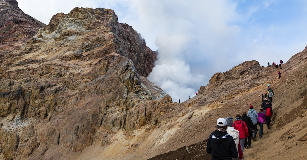 A group of hikers ascend a rugged mountain path surrounded by rocky terrain and dramatic clouds.