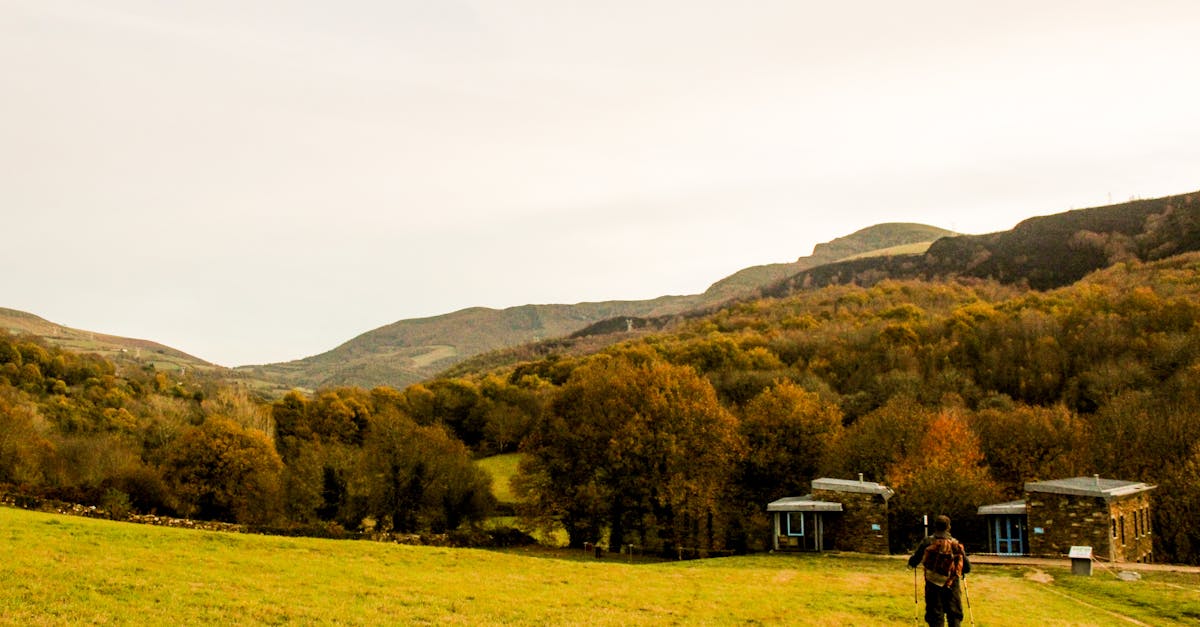 Autumn countryside view with man walking towards picturesque hills and houses, capturing serenity and travel essence.